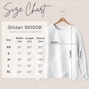 Pode incluir: Uma camisola branca de gola redonda para jovens Gildan 18000B num cabide de madeira. Uma tabela de tamanhos mostra medidas de largura, comprimento e manga em polegadas para tamanhos de XS a XL, com linhas indicando os pontos de medi&ccedil;&atilde;o.