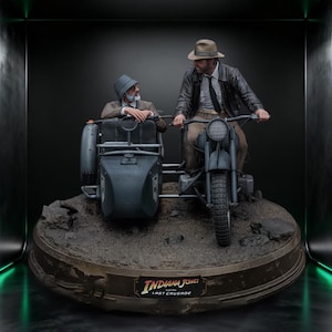 Puede incluir: Una estatua coleccionable detallada que muestra a dos figuras en una motocicleta antigua con sidecar. Una figura lleva un sombrero fedora y chaqueta de cuero, mientras que la otra lleva un sombrero de pescador. La base dice Indiana Jones and the Last Crusade.