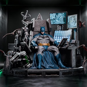 Op de afbeelding: Een gedetailleerd Batman-actiefiguur zittend op een donkere, mechanische troon. Het figuur draagt een grijs en blauw pak met een gele gereedschapsriem. De troon is voorzien van robotarmen, meerdere oplichtende computerschermen met kaarten en gegevens, en vleermuizen.