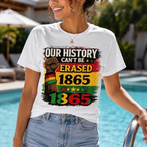 Könnte beinhalten: Ein weißes Kurzarm-T-Shirt mit einem Grafikdruck, der den Text "OUR HISTORY CAN'T BE ERASED 1865" und eine erhobene Faust zeigt. Das Design enthält rote, gelbe und grüne horizontale Streifen sowie kleine Sterne als Akzente.