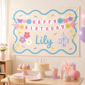 May include: A rectangular fabric banner with a beige background, a wavy blue border, and colorful confetti. It features a "HAPPY BIRTHDAY" garland, the name "Lily" in blue script, and a disco ball graphic. The banner is displayed above a table.