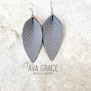 May include: A pair of gray leather earrings with a snake skin pattern. The earrings are in the shape of a teardrop and have silver hooks.