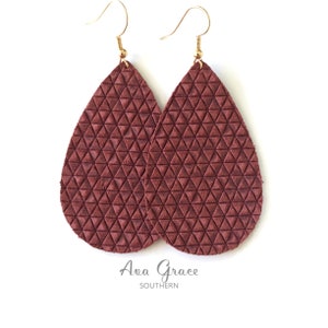 May include: A pair of teardrop-shaped earrings with a geometric pattern. The earrings are made of brown leather and have gold hooks.
