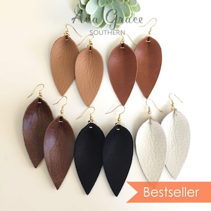 May include: A collection of leaf-shaped earrings in various colors, including tan, brown, black, and white. Each pair features a gold-colored hook. The image includes the text "Ava Grace Southern" and the word "Bestseller".