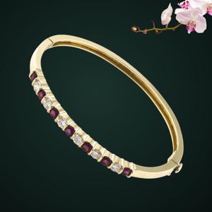 May include: A gold hinged bangle bracelet featuring an alternating row of round-cut deep red rubies and clear white diamonds set along the front section of the band, creating a continuous sparkling pattern against the polished yellow gold metal.