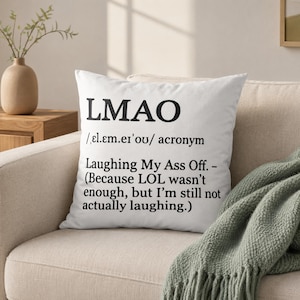 May include: A white square throw pillow featuring black printed text that defines the acronym LMAO. The text includes the phonetic pronunciation, the full phrase Laughing My Ass Off, and the parenthetical note: Because LOL wasn't enough, but I'm still not actually laughing.