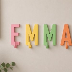 May include: Four wall-mounted hooks shaped like the letters E, M, M, and A. The letter E is pink, the first M is yellow, the second M is light green, and the letter A is orange. Each letter features a small matching hook at the bottom.