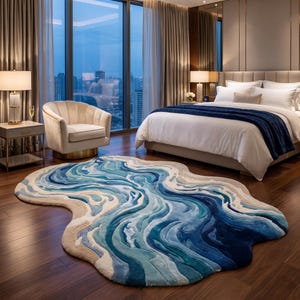 Puede incluir: Una alfombra de forma irregular con un dise&ntilde;o abstracto en capas en tonos azul marino profundo, azul real, turquesa claro y crema. La alfombra presenta un patr&oacute;n ondulado y texturizado que imita el agua fluyendo sobre un suelo de madera.