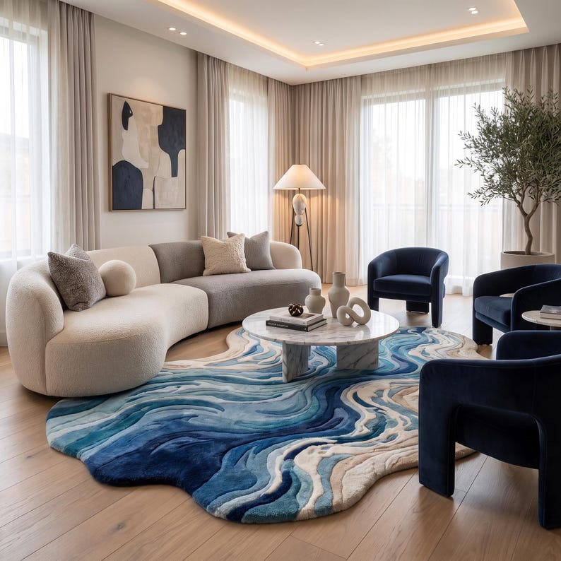 Puede incluir: Una alfombra grande de forma irregular con un patr&oacute;n de ondas en tonos azul, crema y beige. La alfombra tiene una forma fluida y org&aacute;nica, y se encuentra debajo de una mesa de centro redonda de m&aacute;rmol blanco, un sof&aacute; curvo crema y varios sillones azul oscuro.