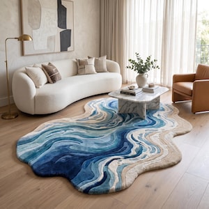 Puede incluir: Una alfombra de forma org&aacute;nica irregular con un dise&ntilde;o topogr&aacute;fico en capas en tonos azul marino profundo, azul real, azul claro y beige arena, que imita la apariencia de las olas del oc&eacute;ano sobre un suelo de madera.