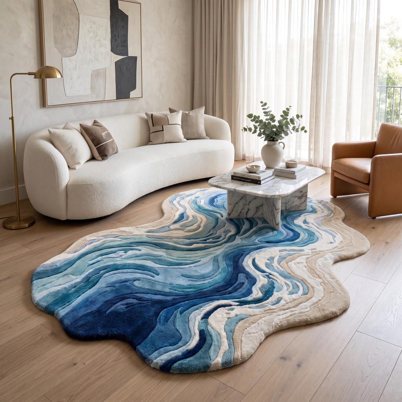 Puede incluir: Una alfombra de forma org&aacute;nica irregular con un dise&ntilde;o topogr&aacute;fico en capas en tonos azul marino profundo, azul real, azul claro y beige arena, que imita la apariencia de las olas del oc&eacute;ano sobre un suelo de madera.