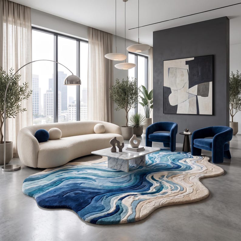 Puede incluir: Una alfombra de forma org&aacute;nica e irregular con un dise&ntilde;o texturizado en capas en tonos azul profundo, azul claro y crema, que imita la apariencia de las olas del oc&eacute;ano encontr&aacute;ndose con la orilla, sobre un suelo de hormig&oacute;n gris liso.
