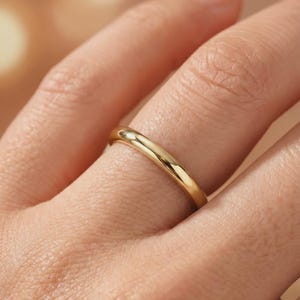 May include: A polished gold band ring with a smooth, rounded surface and a high-shine finish. The ring features a simple, continuous circular design with no additional embellishments, stones, or engravings, showcasing a classic, solid metal construction.
