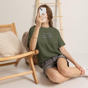 Könnte beinhalten: Ein olivgrünes Kurzarm-T-Shirt mit dem aufgedruckten Text "WARNING: MAY TALK ABOUT POLE" in dunkler Schrift auf der Brust. Das Shirt wird mit einer dunkelgrauen Jeansshorts kombiniert, was einen lässigen Alltagslook ergibt.