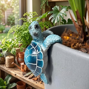 May include: A blue sea turtle figurine with a glossy, textured shell and detailed scales, designed to hang over the edge of a large gray planter. The turtle features shades of light and dark blue with white outlines on the shell segments.