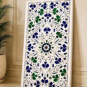 Könnte beinhalten: Eine rechteckige weiße Marmorplatte mit einem komplexen eingelegten Blumenmuster. Das Design besteht aus leuchtend blauen und tiefgrünen Steinblütenblättern und Blättern, die in einem symmetrischen, sich wiederholenden botanischen Motiv angeordnet sind.