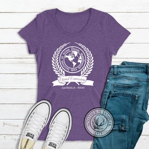 Puede incluir: Camiseta morada de manga corta con un gr&aacute;fico blanco de un globo terr&aacute;queo rodeado de una corona de laurel y el texto "Cum Lacte et Rosse Deum Manifestrum", "Classical Conversations" y "Gatesville - Texas".