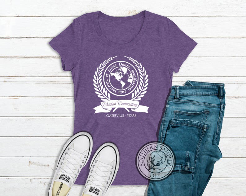 Puede incluir: Camiseta morada de manga corta con un gr&aacute;fico blanco de un globo terr&aacute;queo rodeado de una corona de laurel y el texto "Cum Lacte et Rosse Deum Manifestrum", "Classical Conversations" y "Gatesville - Texas".