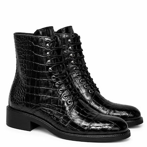 Puede incluir: Un par de botines negros con una textura brillante de imitación de cocodrilo, punta redondeada y cordones frontales con ojales metálicos plateados. Los botines tienen un tacón bajo de bloque y una suela negra a juego.