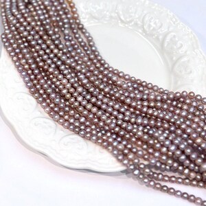 May include: A long strand of small, round, mauve-colored freshwater pearls arranged in multiple rows. Each individual pearl features a smooth, lustrous surface with subtle iridescent undertones, creating a uniform and consistent appearance throughout the strand.