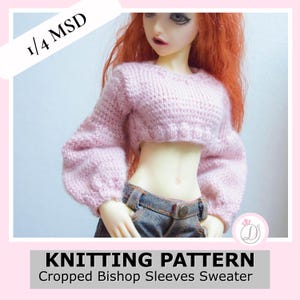 Puede incluir: Un suéter rosa claro, corto, con mangas obispo, usado por una muñeca. El suéter está tejido y tiene un cuello redondo. La muñeca lleva vaqueros. La imagen incluye el texto "KNITTING PATTERN Cropped Bishop Sleeves Sweater".
