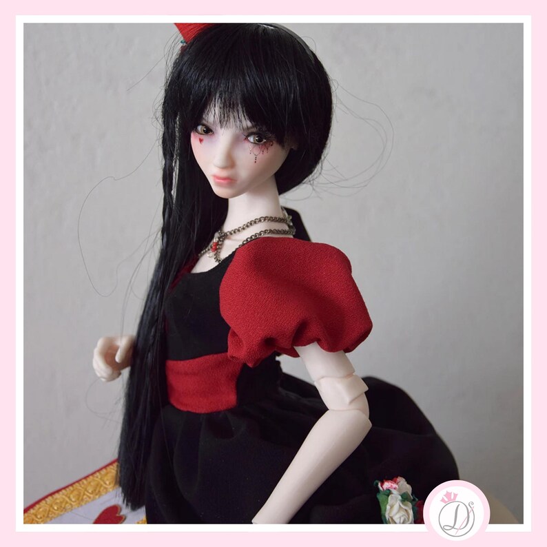May include: A doll with long black hair and a red bow. The doll wears a black dress with red sleeves and a red belt. A silver necklace with a red pendant is around the doll's neck. The doll has pale skin and red accents on the face.