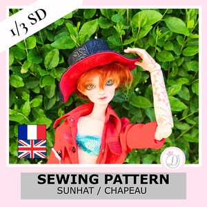 Peut inclure: Une poupée articulée aux cheveux orange portant un chapeau noir et rouge, une chemise rouge boutonnée et un haut crocheté bleu sarcelle. La poupée a un bras à motifs et est devant un feuillage vert. Le texte indique 1/3 SD et SEWING PATTERN.