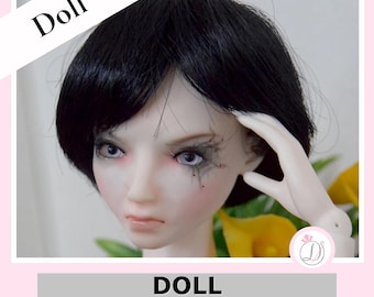 May include: A doll head with short black hair and pale skin. The doll has detailed facial features, including painted eyes and makeup. The text "Doll" is in the upper left corner, and the text "DOLL Olivia face up B" is at the bottom.