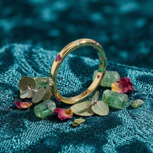 Könnte beinhalten: Ein goldener Bandring mit abwechselnd flach gefassten runden Rubinen und klaren Diamanten. Der Ring ist aufrecht positioniert und zeigt eine glatte, polierte Metalloberfläche sowie ein kreisförmiges Profil mit mehreren Edelsteinfassungen.