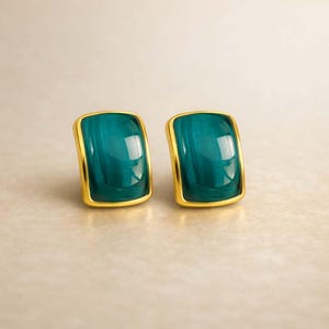 Può includere: Un paio di orecchini a lobo con pietre rettangolari lisce di colore verde acqua intenso, incastonate in montature di metallo color oro lucido. Le pietre presentano una superficie leggermente bombata che riflette la luce in modo lucido.