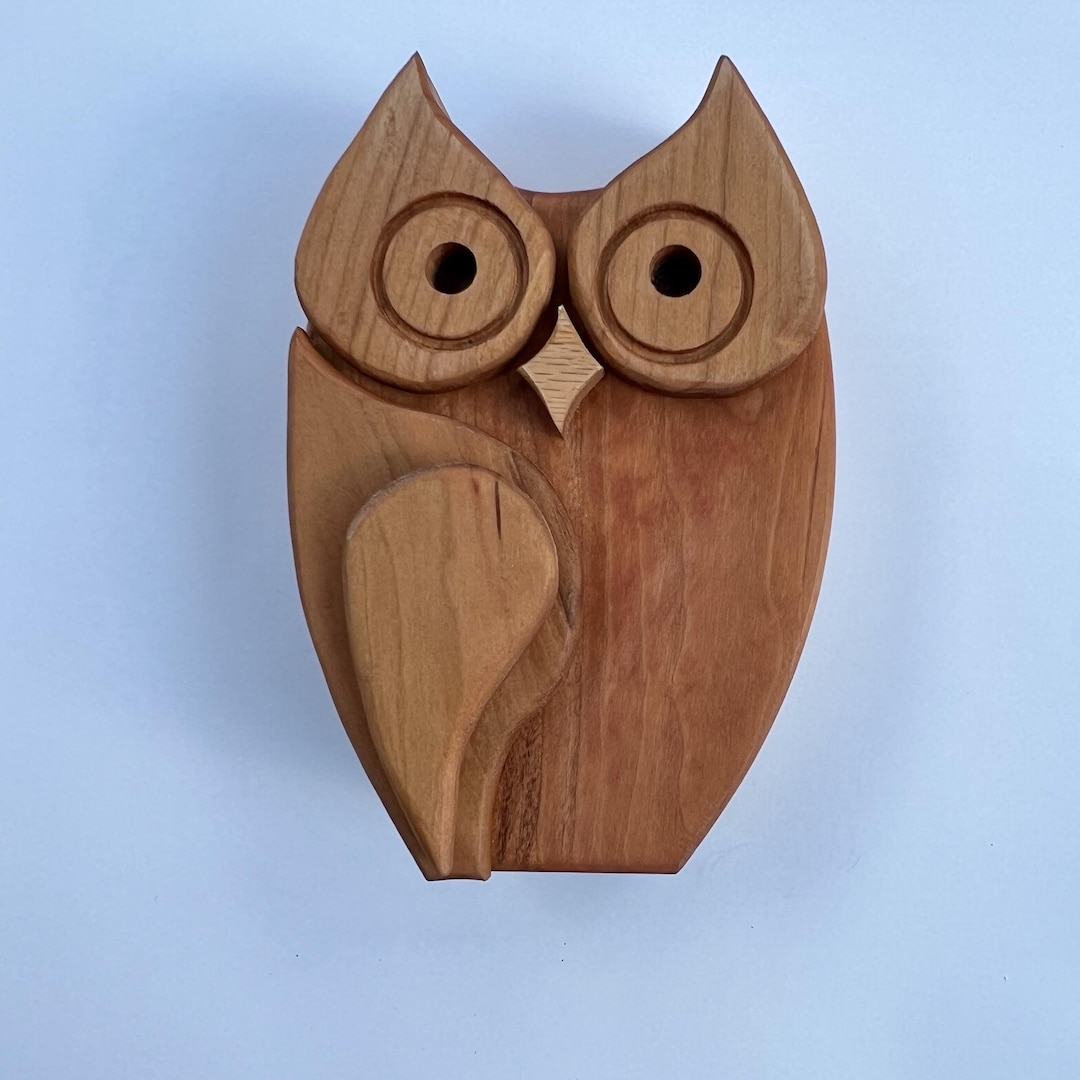 Wooden owl coin bank with round eyes and a heart-shaped wing against a pale blue background