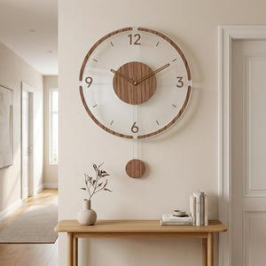 May include: A round wall clock featuring a clear glass face with a wood-toned frame and a central circular wood-toned panel. The clock has gold-colored hands, large numerals at the 3, 6, 9, and 12 positions, and a matching wood-toned pendulum.