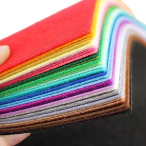 Könnte beinhalten: Ein Stapel rechteckiger Filzblätter in einem lebendigen Farbspektrum, darunter Rot, Orange, Gelb, Grün, Türkis, Blau, Violett, Pink, Grau, Braun und Schwarz. Die Blätter sind ordentlich geschichtet und zeigen das texturierte Fasermaterial.