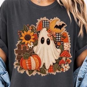 Peut inclure: Un t-shirt gris anthracite avec un motif central repr&eacute;sentant un fant&ocirc;me blanc entour&eacute; d'un design en patchwork compos&eacute; d'une citrouille, d'un tournesol, de champignons rouges, d'un croissant de lune jaune, d'une chauve-souris et d'une cl&ocirc;ture.