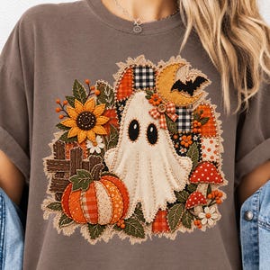 Peut inclure: Un t-shirt gris anthracite avec un motif central repr&eacute;sentant un fant&ocirc;me blanc, une citrouille, un tournesol, des champignons rouges et un croissant de lune. Le design int&egrave;gre des motifs patchwork, des tissus &agrave; carreaux et des d&eacute;tails cousus.