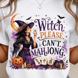 Könnte beinhalten: Ein weißes T-Shirt mit einer Grafik einer Hexe in schwarzem Kleid und Hut, die einen Mahjong-Stein hält. Der Text lautet Witch PLEASE, CAN'T. MAHJONG. Das Design zeigt einen Halbmond, Fledermäuse, einen Kürbis und einen Kessel mit violettem Rauch.