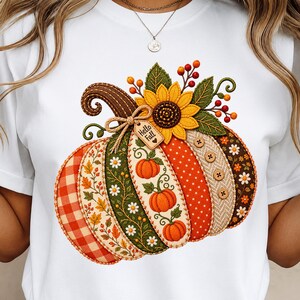 Könnte beinhalten: Ein weißes T-Shirt mit einer großen, farbenfrohen Grafik eines Kürbisses, der aus verschiedenen gemusterten Segmenten wie Karos, Blumen, Punkten und Fischgräten besteht. Eine Sonnenblume, Beeren und ein Etikett mit der Aufschrift Hello Fall sind angebracht.