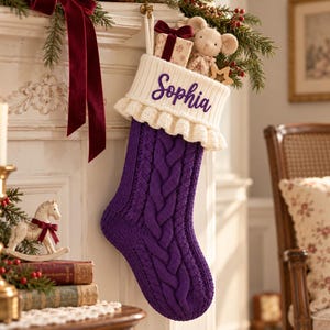 Könnte beinhalten: Ein violetter Weihnachtsstrumpf aus Zopfstrick mit weißem Rüschenbündchen, auf dem der Name Sophia in violetter Schreibschrift gestickt ist. Der Strumpf hängt und enthält eine kleine Geschenkbox sowie eine Plüschmaus mit Stern.
