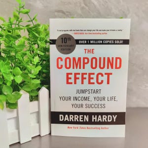 May include: The Compound Effect 10th Anniversary Edition book by Darren Hardy with a white cover, red and black text, and a circular badge stating over 1 million copies sold. The title reads The Compound Effect Jumpstart Your Income, Your Life, Your Success.