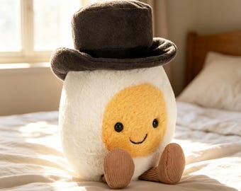 Peluche Jellycat Amuseable Groom a forma di uovo sodo, un simpatico uovo con cappello a cilindro nero, ideale come regalo per matrimoni o addii al celibato.