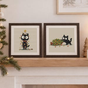 Può includere: Due opere d'arte a punto croce incorniciate di forma quadrata con un gatto nero. La cornice a sinistra mostra un gatto aggrovigliato in luci natalizie colorate con una stella gialla sulla testa. La cornice a destra mostra un gatto nero che spinge un piccolo albero di Natale.