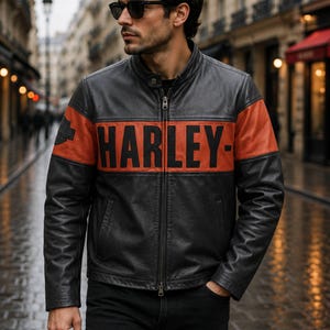 May include: A black leather jacket featuring a horizontal orange stripe across the chest with the word HARLEY printed in bold black letters. The jacket has a stand-up collar, a full-length front zipper, and a small logo patch on the right sleeve.