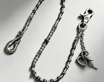 May include: A wallet chain featuring dark faceted beads interspersed with silver-toned metal spacers. One end has a large curved hook, while the other end includes a lobster clasp attached to a small silver snake charm and a short chain link.