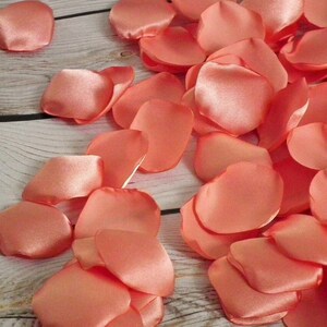 May include: A pile of coral-colored satin rose petals. The petals are soft and delicate, perfect for scattering on a table or floor.