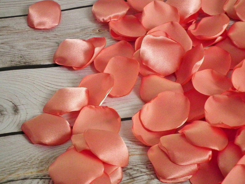 May include: A pile of coral-colored satin rose petals. The petals are soft and delicate, perfect for scattering on a table or floor.