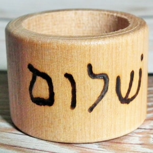 May include: A wooden ring with the Hebrew word "Shalom" inscribed on it. The ring is light brown and has a smooth finish.