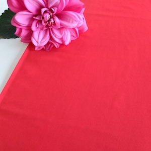 May include: A single pink flower with a red background. The flower is in the top left corner of the image.