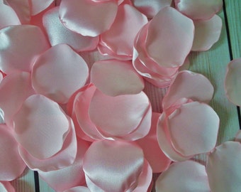 Puede incluir: Un montón de pétalos de rosa de satén rosa claro. Los pétalos son suaves y delicados, perfectos para decorar una boda o un evento especial.