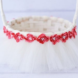 May include: A white basket with a tulle skirt and a pink flower trim. The flowers have pearl accents.