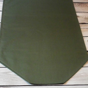 Può includere: Un runner da tavolo verde tinta unita con un'estremità appuntita. Il runner è realizzato in tessuto liscio.